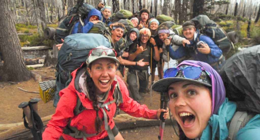 a group of outward bound students carrying backpacks pose excitedly for a photo